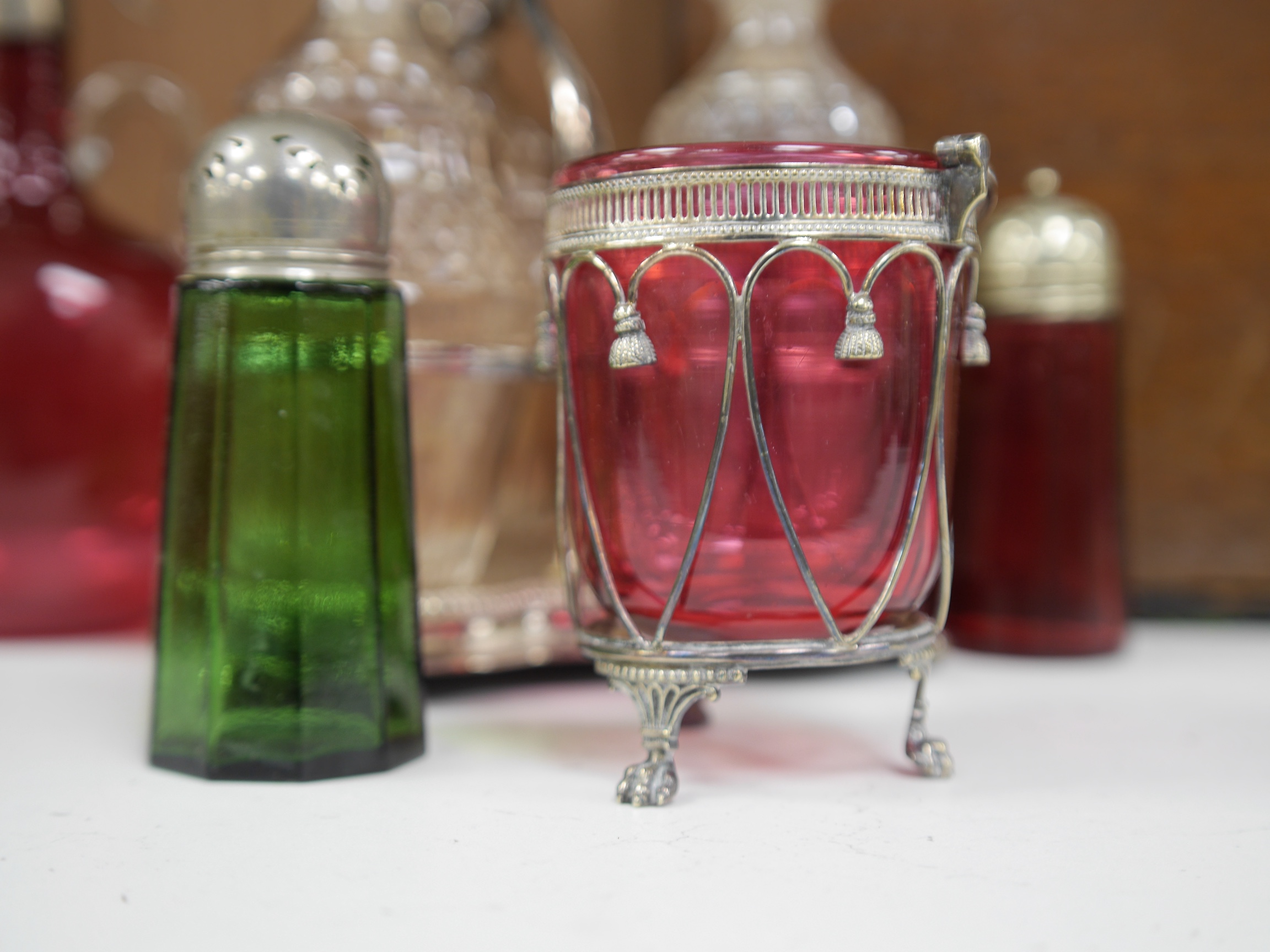 A cased silver plated three bottle liqueur stand, a cranberry decanter, sugar shaker and jam stand together with a green glass shaker, stand 27cm high (5). Condition - all items in good condition, box in need of a clean